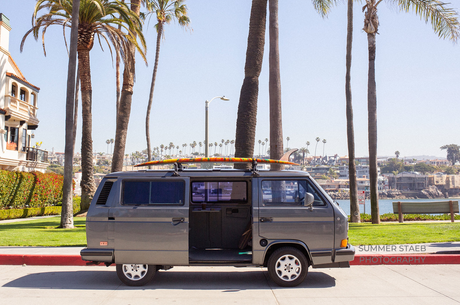 Vintage VW Vanagon RV rental with a surfboard, ideal for coastal adventures & beach life.