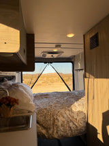 Inviting RV rental interior: a bed with patterned linens, small sink, and mesh screen offering desert mountain views.