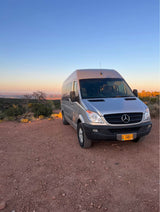 This silver Mercedes Sprinter RV rental camper van enjoys a stunning desert sunset from a dirt road.
