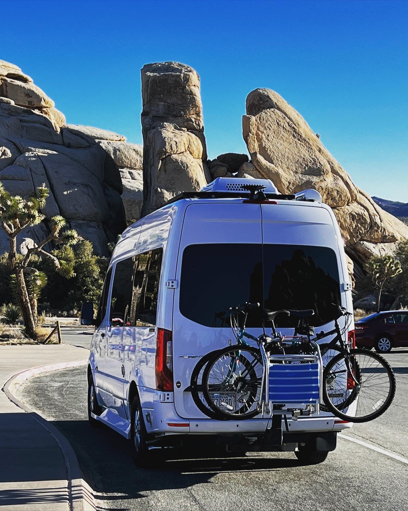 Exploring Joshua Tree: White RV rental with bikes parked amidst majestic rock formations under a clear blue sky.