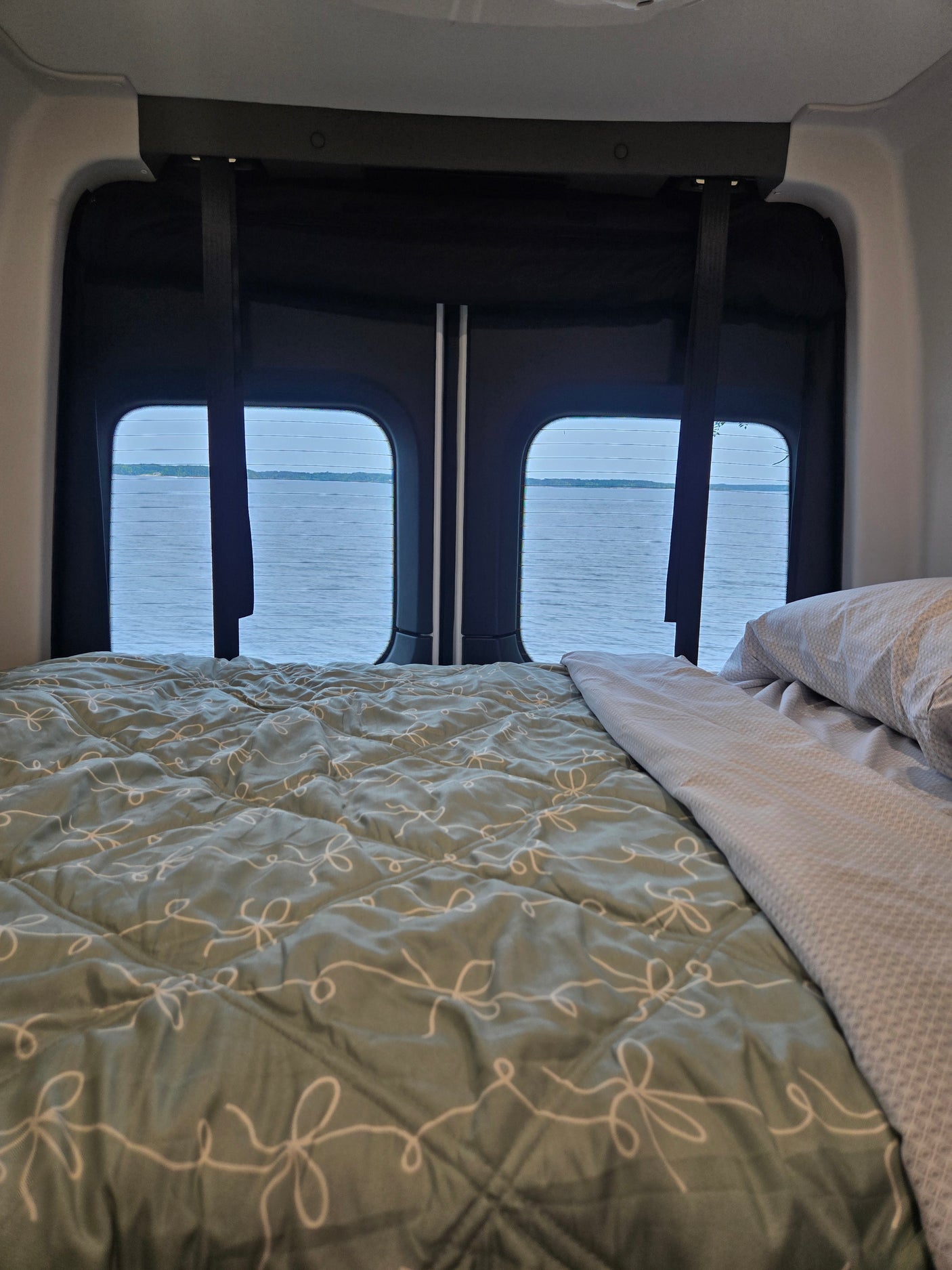 Peaceful rv rental interior: A cozy bed faces large windows with a scenic view of a calm lake.