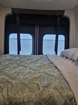 Peaceful rv rental interior: A cozy bed faces large windows with a scenic view of a calm lake.