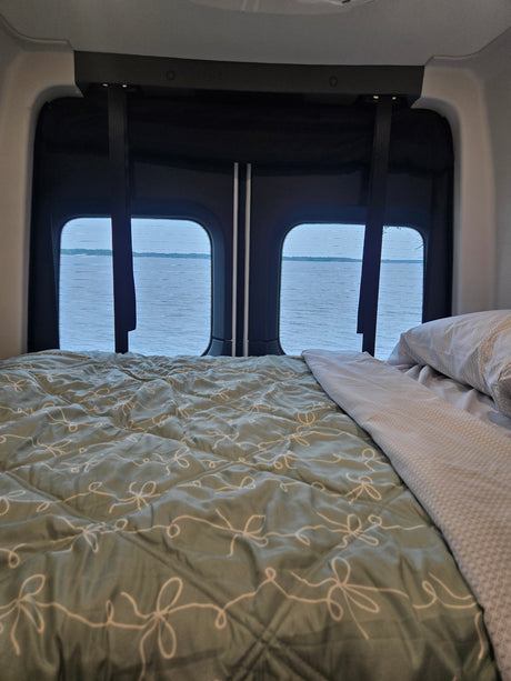 Peaceful rv rental interior: A cozy bed faces large windows with a scenic view of a calm lake.