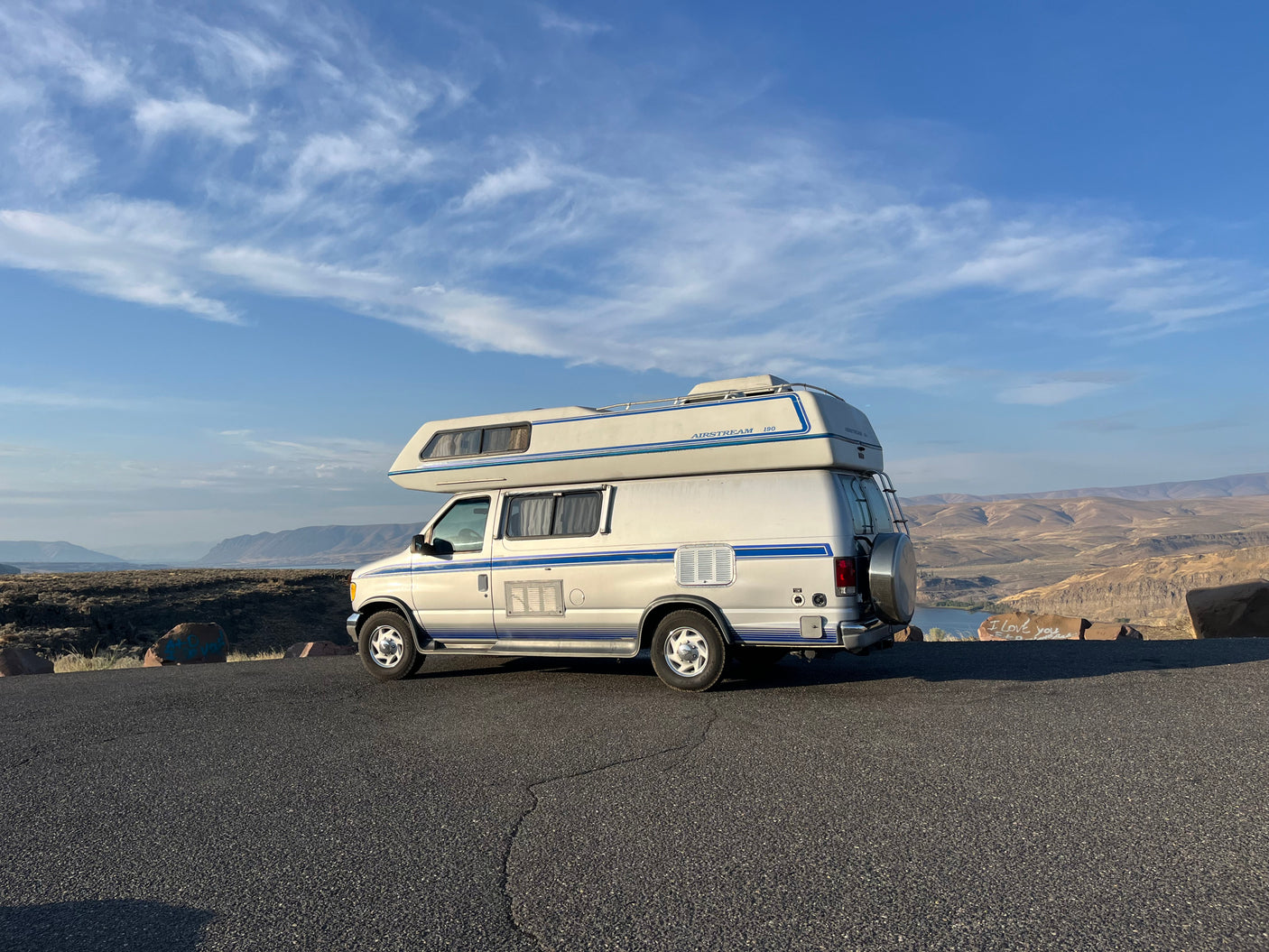 White Airstream 190 RV parked on an asphalt road overlooking a scenic valley with water, ideal for rv rental.