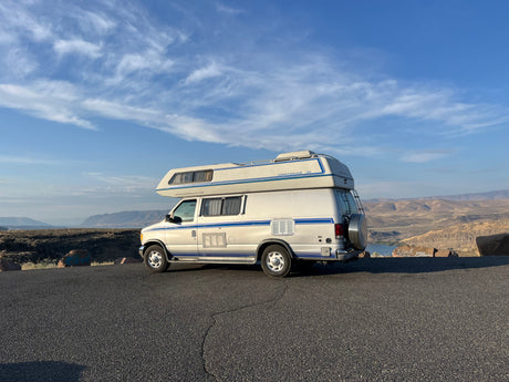 White Airstream 190 RV parked on an asphalt road overlooking a scenic valley with water, ideal for rv rental.