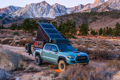 A customized overlanding Toyota Tacoma with a pop-up camper, perfect for an RV rental mountain adventure.