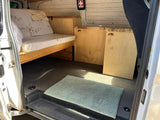 Inside a well-appointed Mercedes-Benz RV rental. Features custom bed/couch, wooden cabinets, and a neat interior.