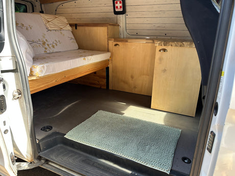 Inside a well-appointed Mercedes-Benz RV rental. Features custom bed/couch, wooden cabinets, and a neat interior.
