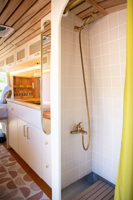 Stylish RV rental interior with compact shower, brass fixtures, and kitchenette. Perfect for cozy van life adventures!
