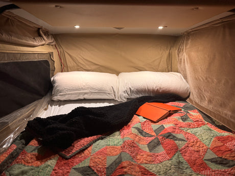 Cozy RV rental bed setup with white pillows, a colorful quilt, and an open journal, ideal for a relaxing night.