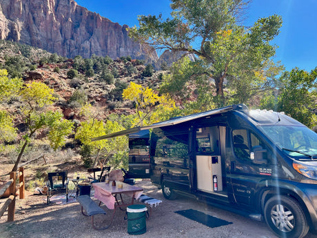RV rental set up for glamping amidst stunning red rock mountains and vibrant autumn foliage at a scenic campsite.