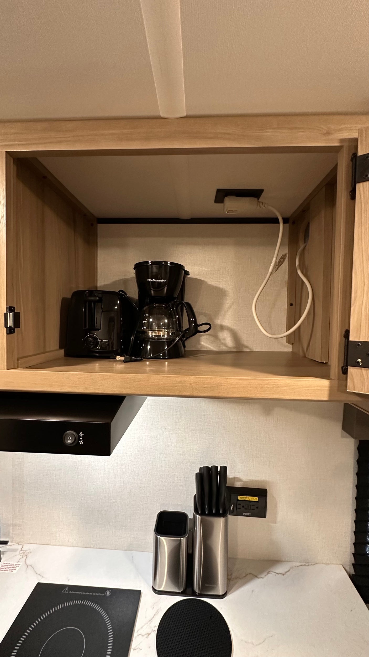 RV rental kitchen: light wood cabinet with black toaster/coffee maker; induction cooktop & knife block on the counter below.