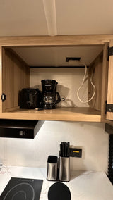 RV rental kitchen: light wood cabinet with black toaster/coffee maker; induction cooktop & knife block on the counter below.