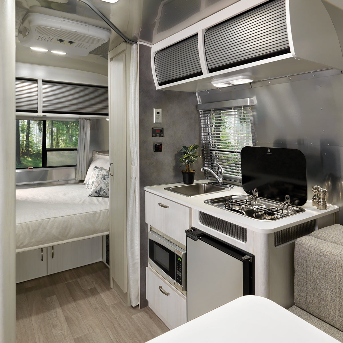 Inside this RV rental, find a modern kitchen (stove, fridge, sink) connecting to a cozy bedroom with forest views.