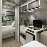Inside this RV rental, find a modern kitchen (stove, fridge, sink) connecting to a cozy bedroom with forest views.