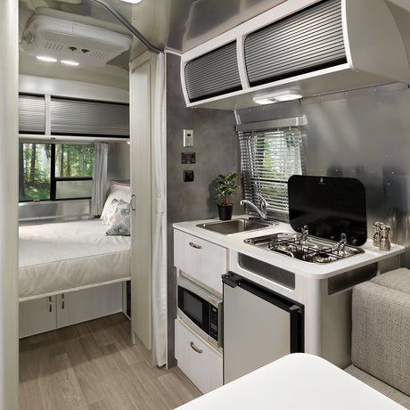 Inside this RV rental, find a modern kitchen (stove, fridge, sink) connecting to a cozy bedroom with forest views.