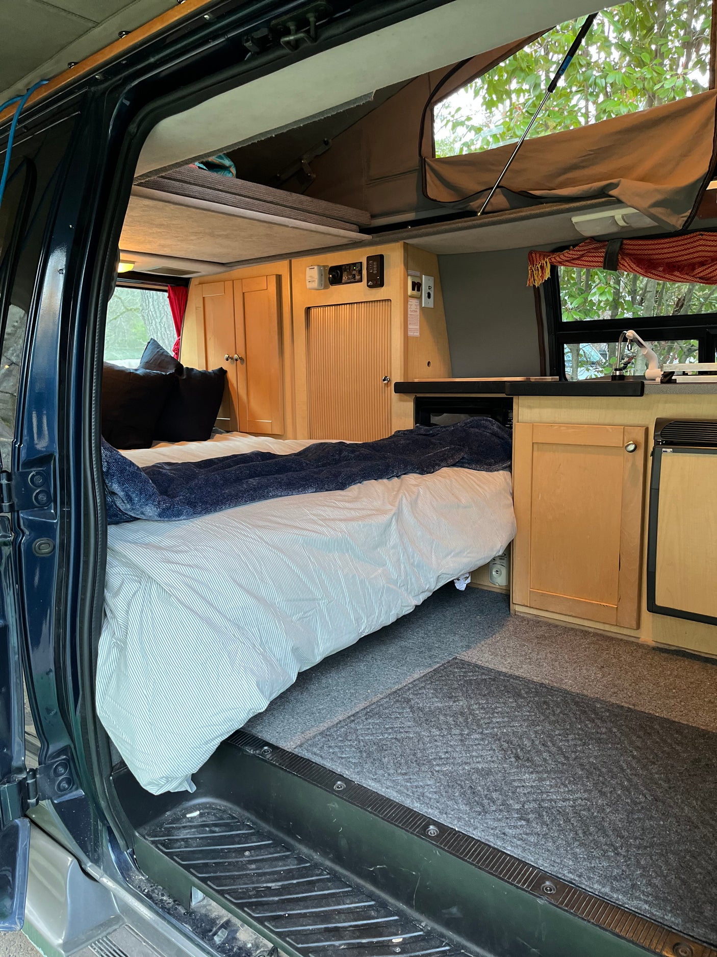 Cozy RV rental interior: pop-top camper with bed, kitchen, and ample storage, perfect for your next adventure.