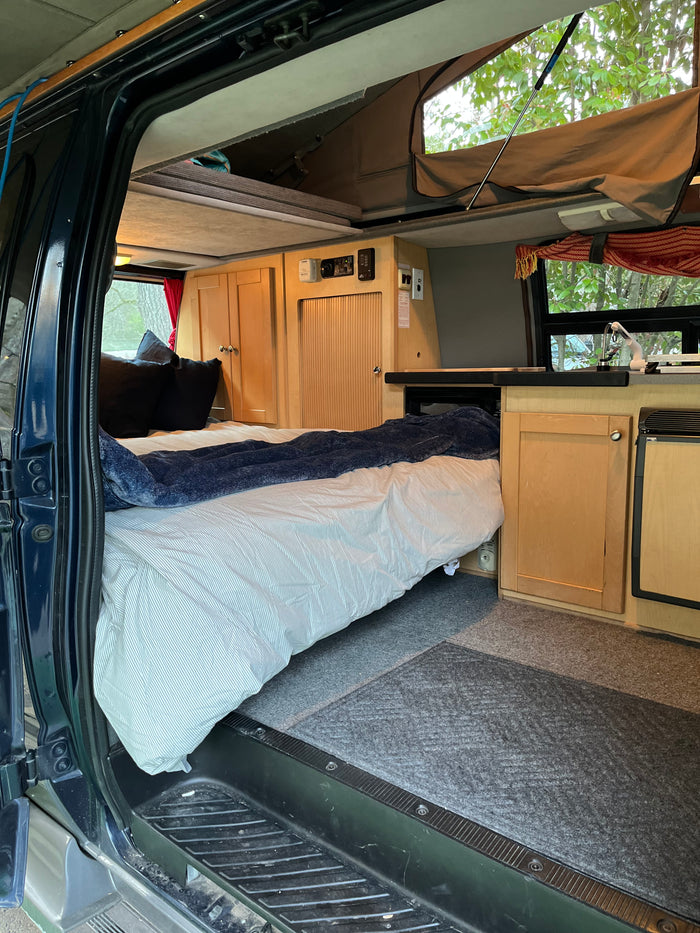 Cozy RV rental interior: pop-top camper with bed, kitchen, and ample storage, perfect for your next adventure.