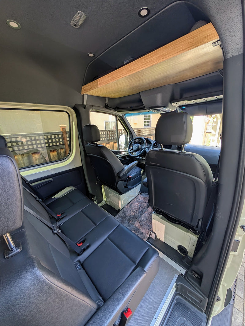Interior of an RV rental van featuring multiple rows of black leather seating and a wooden overhead storage shelf. — photo 3