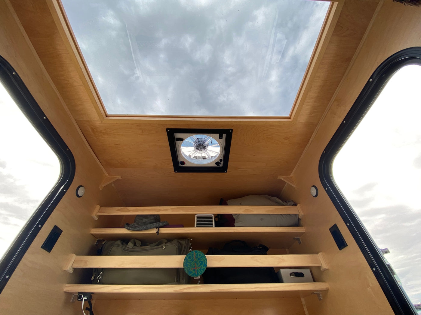 Compact RV rental interior featuring a large overhead skylight, ceiling fan, and practical storage shelves for gear. — photo 9