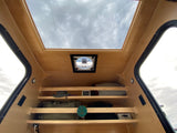 Compact RV rental interior featuring a large overhead skylight, ceiling fan, and practical storage shelves for gear.
