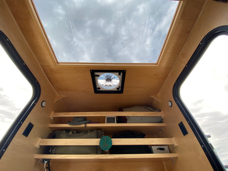 Compact RV rental interior featuring a large overhead skylight, ceiling fan, and practical storage shelves for gear.