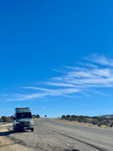 A grey Mercedes-Benz Sprinter rv rental parked by a rural highway, ready for adventure under a clear blue sky.