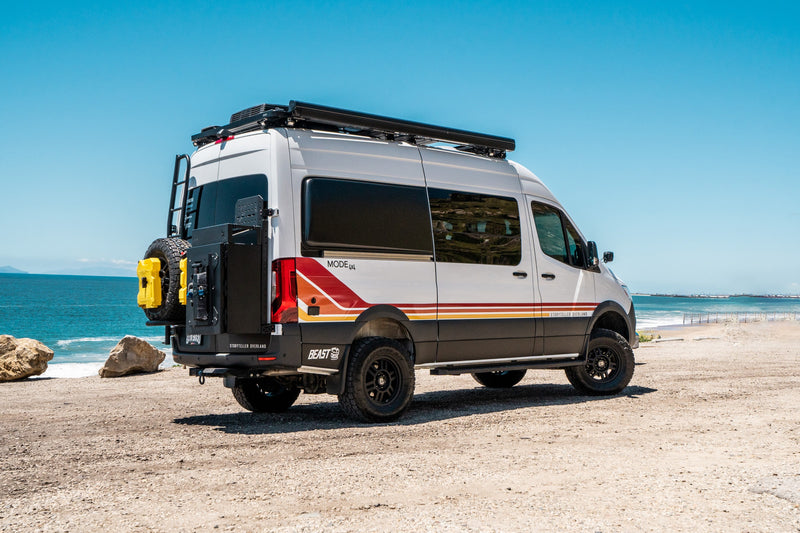 White Storyteller Overland RV rental van, equipped for adventure, parked on a beach with the ocean visible. — photo 9