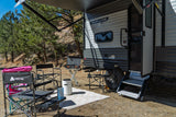 An RV rental for outdoor leisure: a travel trailer with an extended awning, camping chairs, grill, and fire pit.