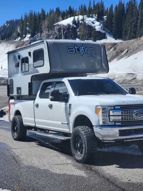 This rugged Ford Super Duty with an Atom truck camper, perfect for an RV rental adventure, is ready for mountain exploring.