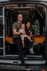 Smiling family inside a custom RV rental. A dad holds a toddler, an older child sits beside them in the camper van.
