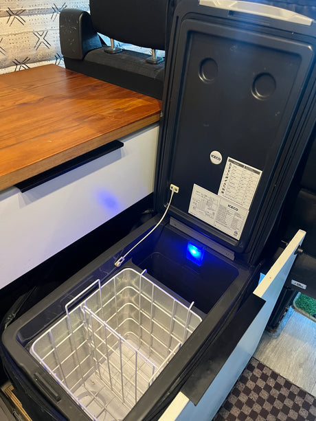 An open ICECO portable fridge/freezer with an internal basket and blue light, perfect for an RV rental adventure.