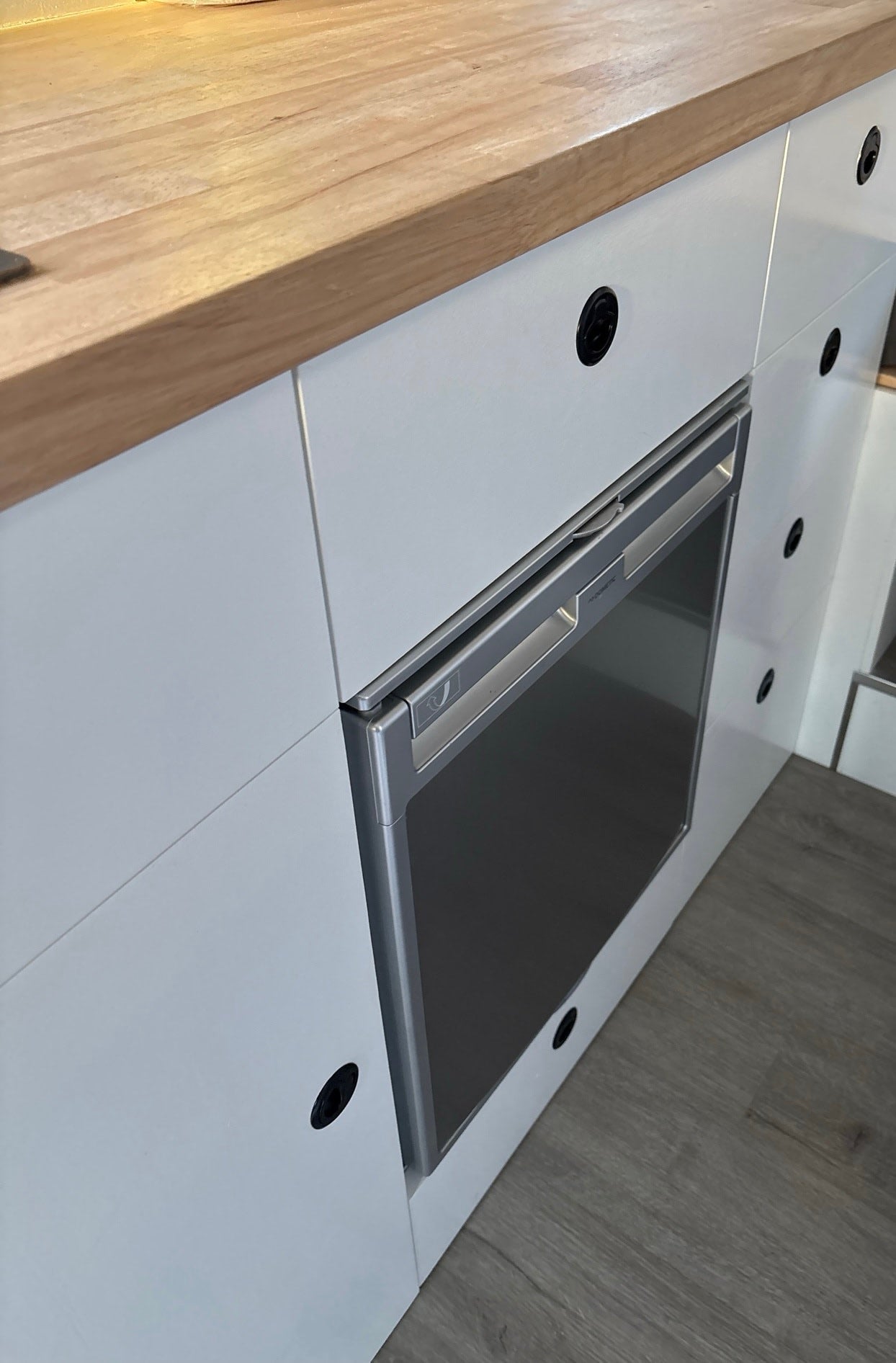 Compact fridge & wood counter in a modern RV rental kitchenette, perfect for road trips.