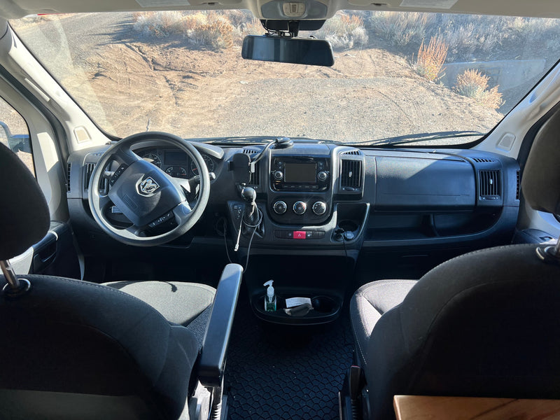 View from an RV rental cabin, showing the dashboard, steering wheel, and front seats, looking out onto a dry, unpaved road. — photo 9