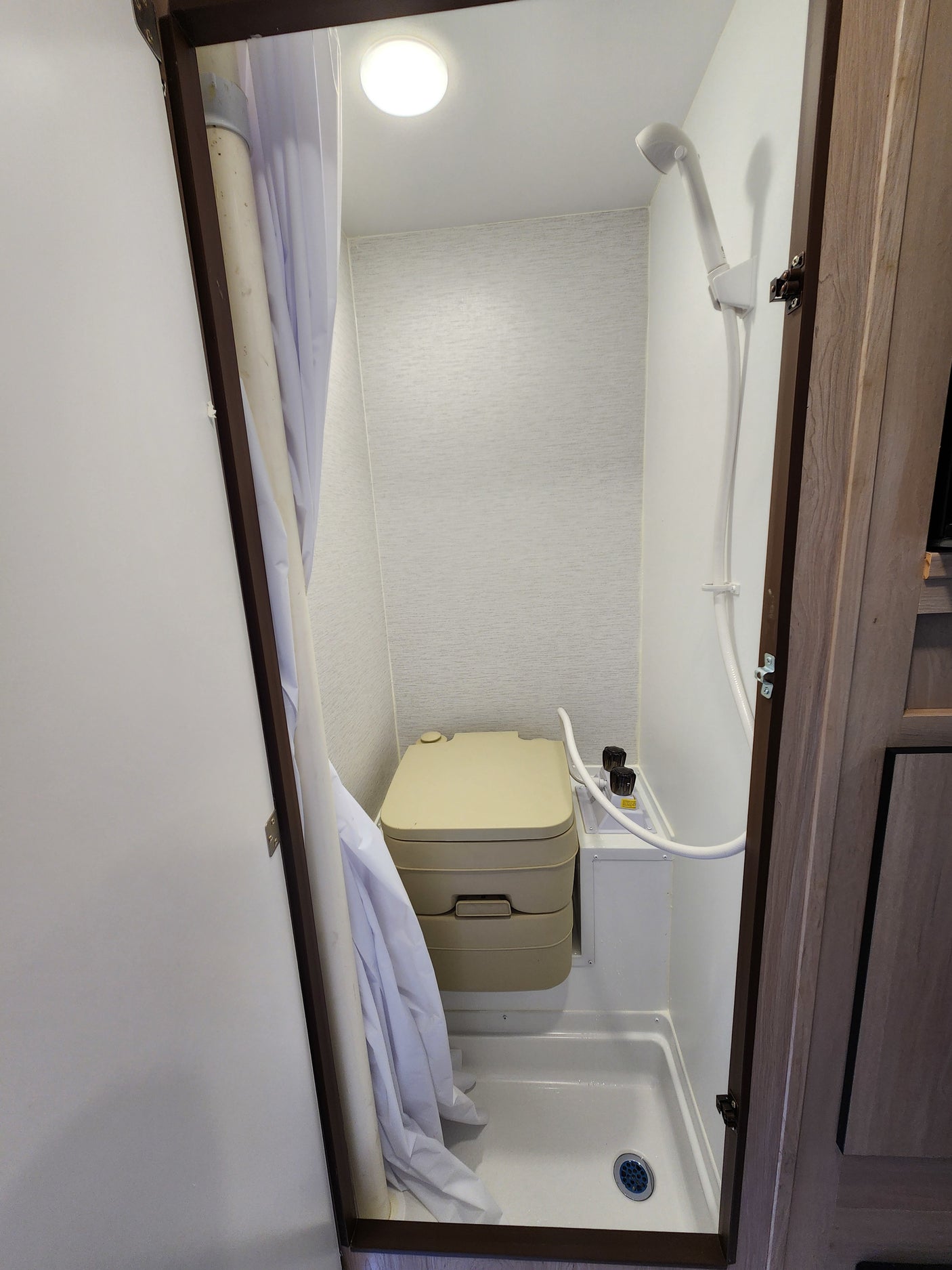 Compact RV rental wet bath features a portable toilet, shower, and a white shower curtain to the left.