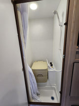 Compact RV rental wet bath features a portable toilet, shower, and a white shower curtain to the left.