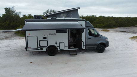 RV rental: A modern white and grey EKKO camper van with an extended pop-top and awning, parked on sand.