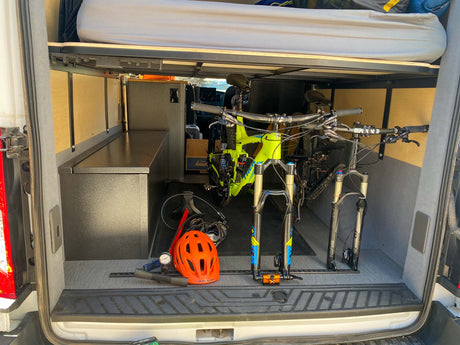 Organized RV rental storage: mountain bikes secured below the bed in a custom van setup. Adventure ready!
