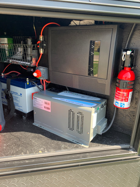 RV rental compartment showing an electrical power system: batteries, Renogy inverter, WFCO panel, and fire extinguisher.