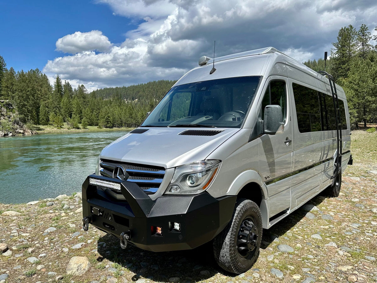 Silver Mercedes Sprinter RV rental showcasing adventure readiness by a river. This converted van with off-road features is ideal for nature trips.|Silver Sprinter van rv rental with off-road gear parked by a river