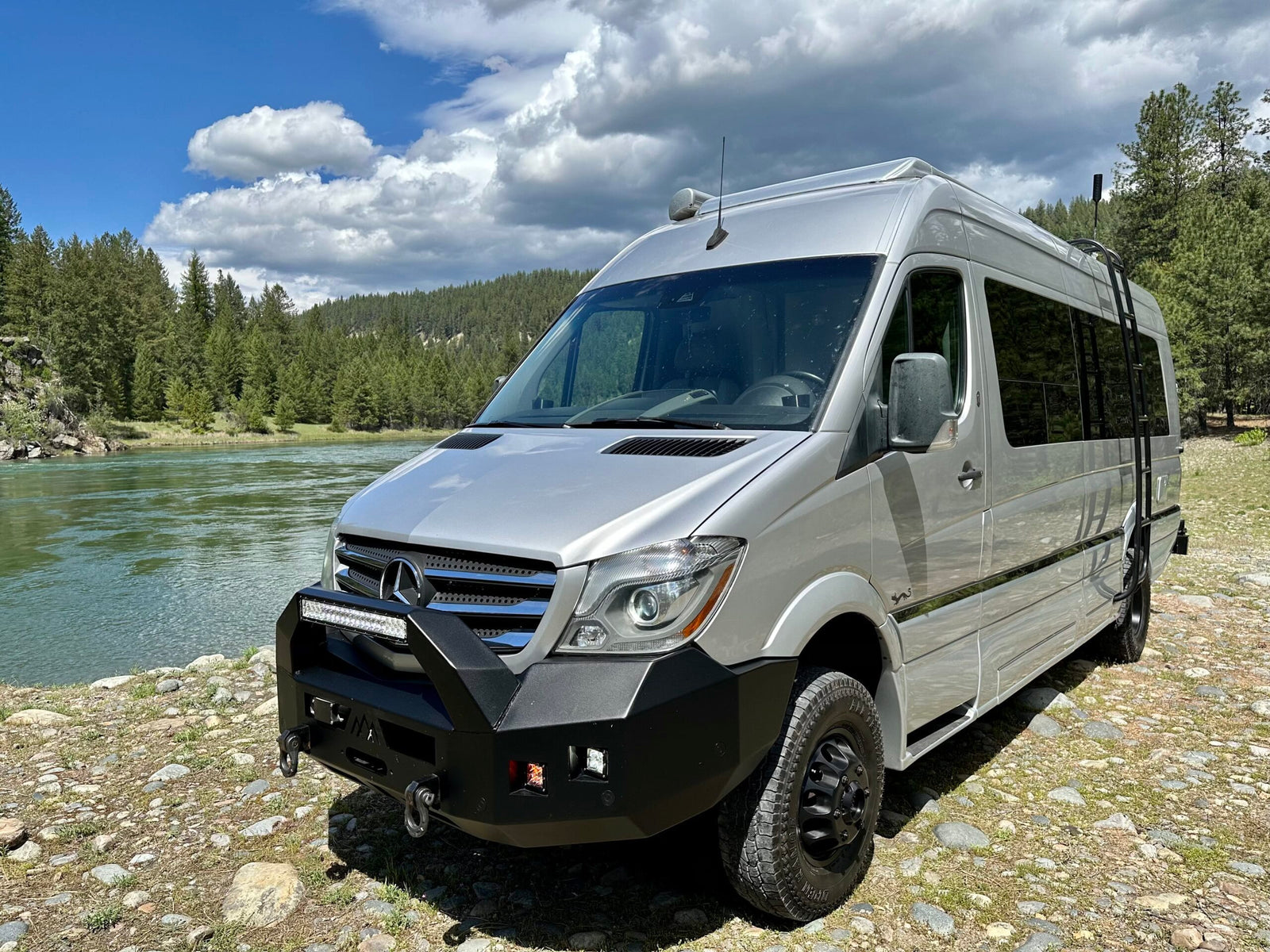 Silver Mercedes Sprinter RV rental showcasing adventure readiness by a river. This converted van with off-road features is ideal for nature trips.
