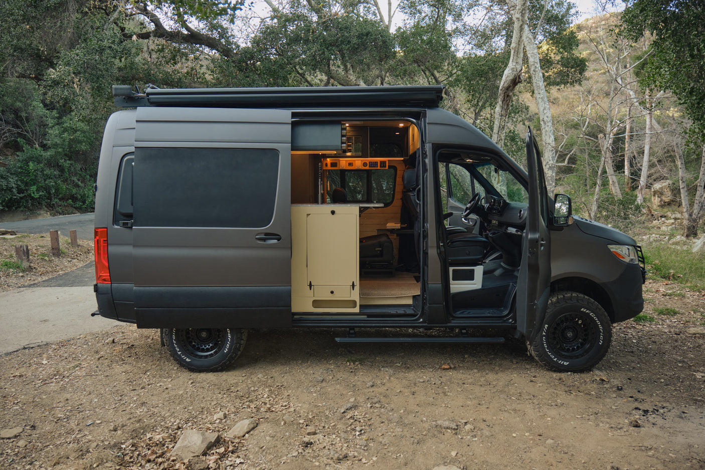 Ready for adventure: a dark grey rv rental camper van, parked in nature, showcases its custom, illuminated interior via open doors.