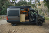 Ready for adventure: a dark grey rv rental camper van, parked in nature, showcases its custom, illuminated interior via open doors.