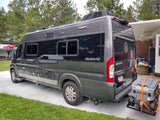 Dark grey Travato RV rental, a Class B camper van, is parked with a cooler on a rear cargo carrier.