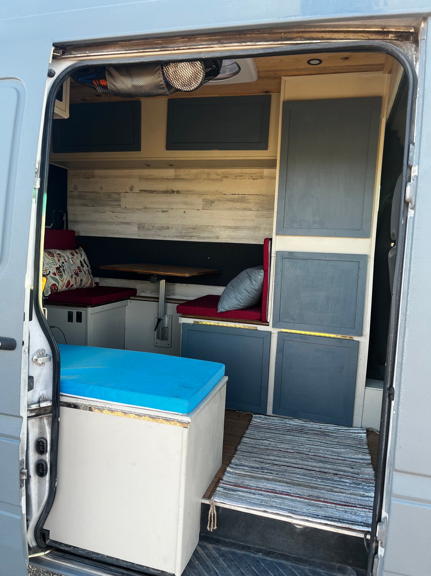 Step inside this cozy rv rental: a compact interior featuring a dining nook, storage, and bed with blue cushion.