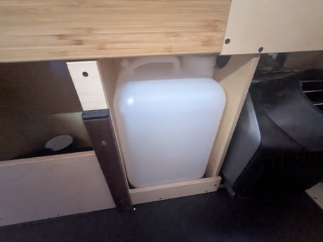 RV rental: Water jug stored in a wooden compartment, providing essential utility for camper living.