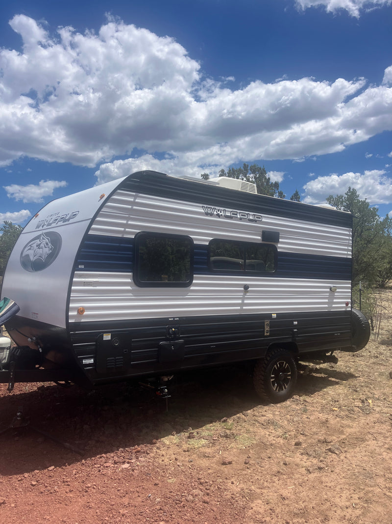 A compact Wolf Pup travel trailer, ideal for an rv rental, is parked outdoors on red earth under a bright, cloudy sky. — photo 1