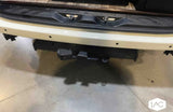 Rear of an RV rental, featuring a white bumper with parking sensors, a trailer hitch receiver, and electrical connector.