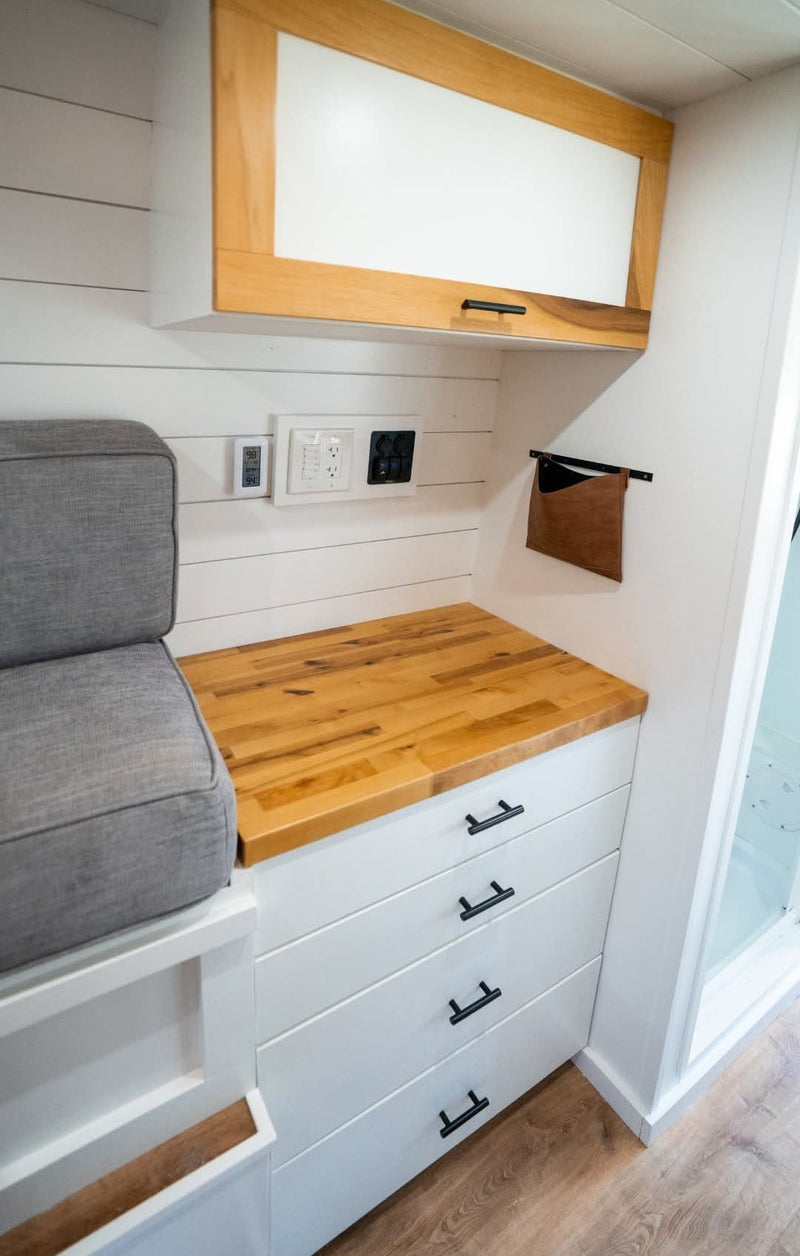 Modern RV rental interior: white shiplap walls, wood countertop, storage drawers, overhead cabinet, and comfy seating. — photo 16