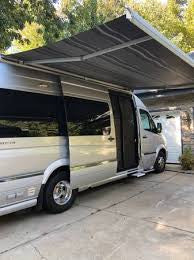 Silver camper van RV rental with extended awning & open screen door on driveway by garage, ready for adventure. — photo 10
